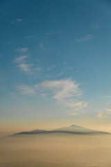 Winter landscape with snow capped mountain peak under sunlight and blue sky with clouds