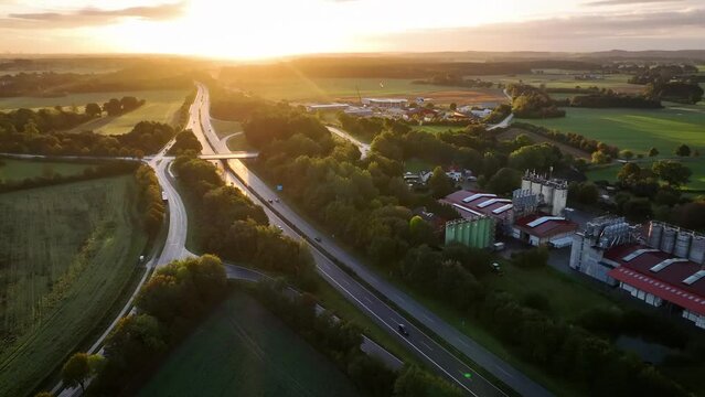 Aerial footage in the morning hours traffic flow over a bustling highway with interchange. Transportation hub near manufacturing facility for natural fiber industry, industrial zone and country side. 