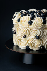 Beautiful cake with white whipped cream cheese curls decorated with blueberries on the black background. Buttercream swirls on the birthday cake