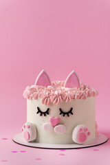 Cute birthday cake in the shape of cat with mastic ears and paws decorated with pink cream fur on...