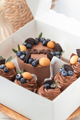 Birthday white gift box with brown chocolate mini bento cake and cupcakes decorated with cookies and blueberries on the white background