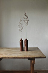 Minimalist artistic composition. Fragments of an old country house interior design - plastered lighted walls, an ancient wooden table, clay glazed bottles, bent plant. Bright and cozy wallpaper