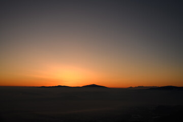Panoramic view during sunset over snow cladded mountain peaks covered with smoky fog