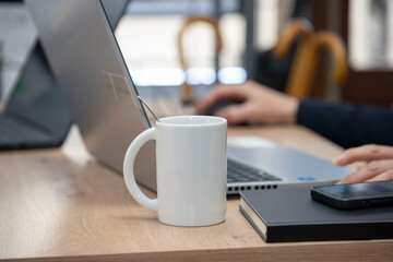 tasse ou mug blanc posé sur un bureau à coté d'un ordinateur portable