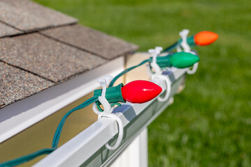 Hanging Christmas string lights on gutter of house. Holiday decorating safety, lighting and accident prevention concept.