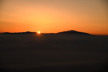Mesmerizing view of the sun setting behind sharp mountain peaks shrouded in mist