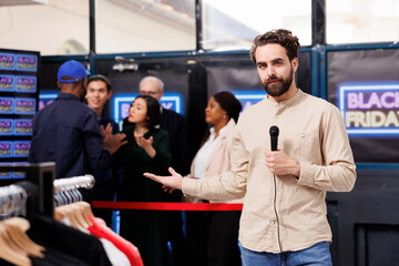 TV reporter gesturing showing shopper crowd to camera while reporting live on Black Friday sales in...