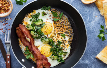 A close look into a fry pan of cheddar fried eggs with a herb salad and bacon.