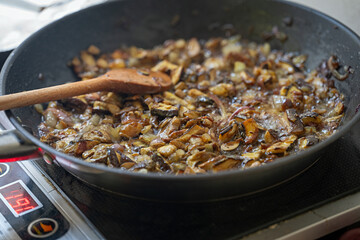 A wooden spatula on a pan with frying mushrooms.