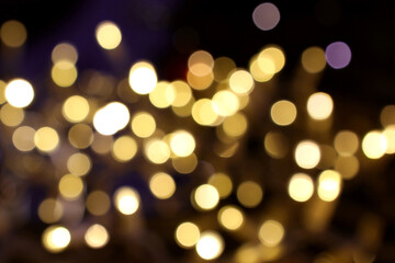 Yellow blurred bokeh lights of holiday decoration illumination in city. Abstract background with Christmas tree garland warm lights. Shiny defocused bokeh circles, dark blue backdrop.