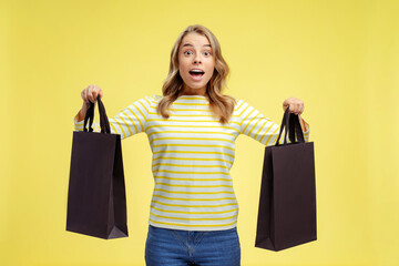 Fototapeta na wymiar Portrait of beautiful excited woman holding black shopping bags isolated on yellow background, mockup. Shopping, sale, black Friday concept