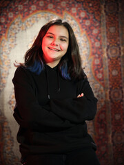 Portrait of beautiful teenage girl with brunette hair. Confident girl wearing black dress while posing at Turkish Carpet background. Copy space.