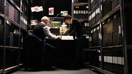 Team of experts read case files in police incident room, using confidential documents and records. Law enforcement officers reviewing evidence authenticity, uncover clues. Tripod shot.