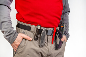 Pen, walkie-talkie, knife and flashlight with clips on the waistband of trekking pants. EDC items