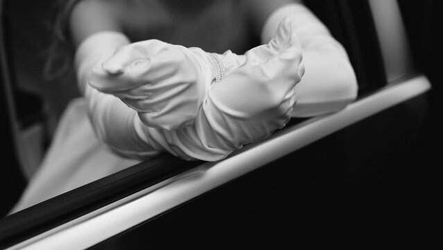 A girl in beautiful stylish white gloves is sitting in a car. She leaned her hands on the door and poses for the camera