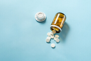White medical pills and tablets spilling out of a drug bottle. Macro top down view with copy space.