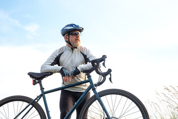 Obraz premium Bearded man cyclist stands with a bike against the blue sky. cycling and health hobbies