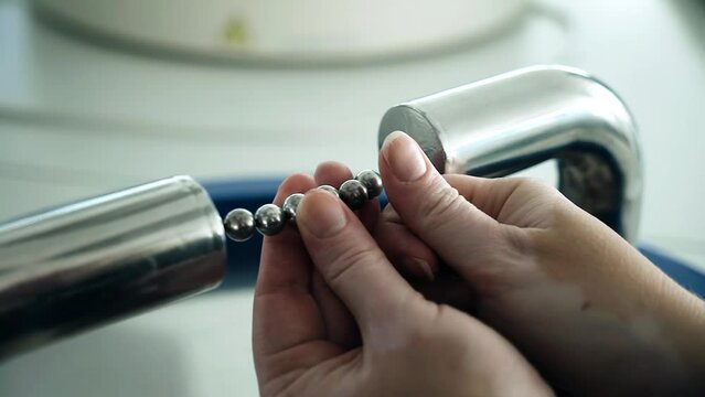 The girl makes experiments with metal balls. The balls are located between two magnets. Practical physics.