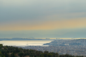 Panorama of the city of Athens taken from the mountain, cargo ships waiting to enter the port, many urban residential buildings.  View at sunset.