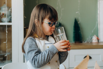 A girl with Down syndrome drinks orange juice and sits at the table on Christmas Eve.