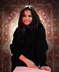 Portrait of smiling teenage girl looking at camera with happiness. Wonderful model with brunette hair posing in studio. A Happy and teenage girl portrait. Ethnic Turkish Carpet in the background