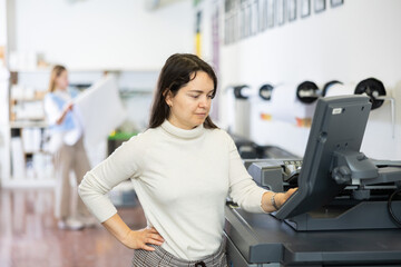 Fototapeta na wymiar Caucasian woman working in printing office, using large format printer.