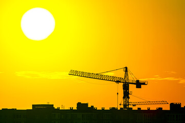 Construction cranes with built houses on the background of the sunset sky