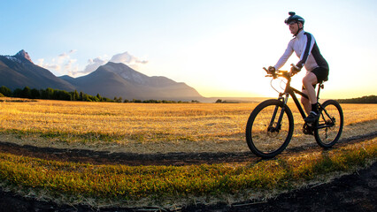 The cyclist rides a bike on the road near the field against the backdrop of the setting sun....
