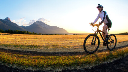Fototapeta premium The cyclist rides a bike on the road near the field against the backdrop of the setting sun. Outdoor sports. Healthy lifestyle.