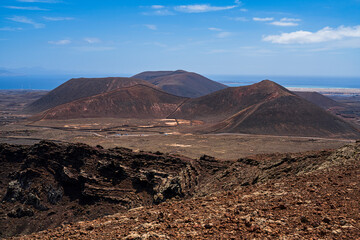 View of a corner of the crater of one of the most famous volcanoes on the island and in the background the sea with several more volcanoes. Photography taken in Fuerteventura, Canary Islands, Spain.