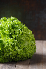 A large bunch of fresh lettuce leaves on a wooden table and a dark background.