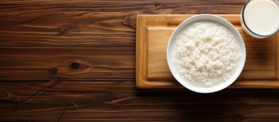 The plate of white rice and creamy porridge is beautifully arranged on the wooden table with a glass of milk placed directly above creating a stunning top view in close up