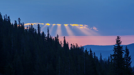 the rays of the sun pass through the clouds against the backdrop of forests and mountains.