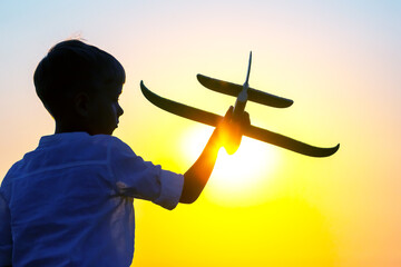 silhouette of a boy lets a model plane fly into the sky against the backdrop of the setting sun....