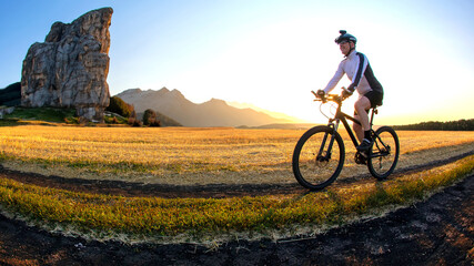 Obraz premium The cyclist rides a bike on the road near the field against the backdrop of the setting sun. Outdoor sports. Healthy lifestyle.