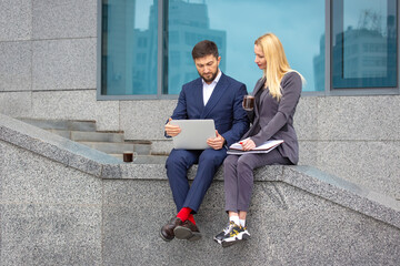 Communication of business partners in an urban setting. successful businessmen man and woman with documents and laptop in hands discuss business projects. Business and trust at work