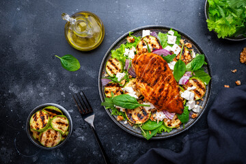 Fresh salad with grilled  zucchini and chicken breast, soft cheese, walnuts, red onion and spinach, black table background, top view