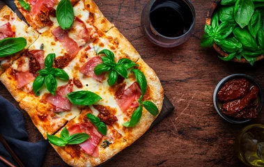 Fototapeten Rectangular roman pizza with smoked ham, mozzarella cheese, sun dried tomatoes, tomato sauce and green basil leaves on rustic wooden table background, top view © 5ph