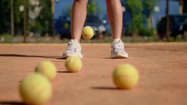 A girl tennis player stands on the sports field and practices hitting the ball with a racket on the ground. The training of impact force. Close up. The blur effect.