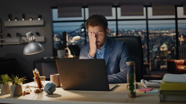 Tired man working laptop evening office closeup. Businessman reading computer