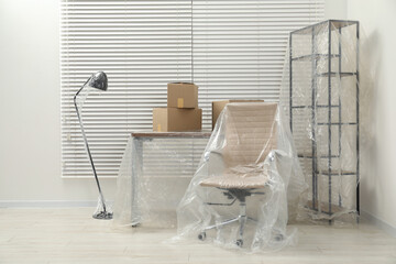 Modern furniture covered with plastic film and boxes at home