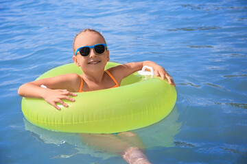 Happy little girl with sunglasses and inflatable ring in sea on sunny day. Beach holiday