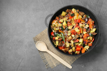 Delicious ratatouille in baking dish and wooden spoon on grey table, flat lay. Space for text