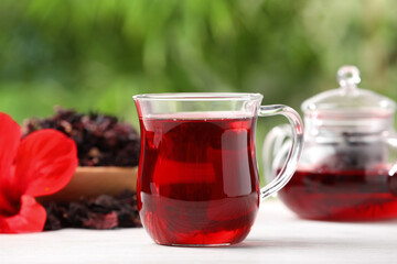 Glass cup of delicious hibiscus tea on white wooden table outdoors, closeup