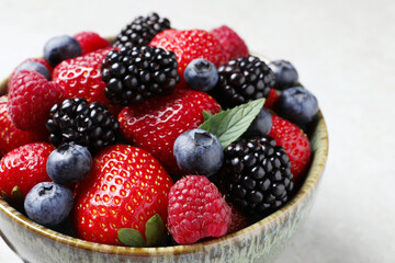 Different fresh ripe berries in bowl on table, closeup
