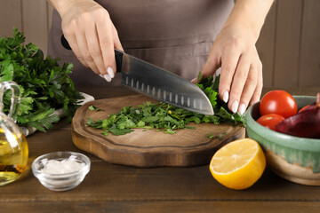 Woman cutting fresh parsley at wooden table, closeup