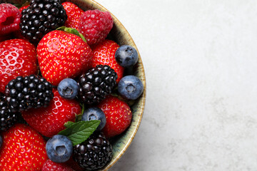 Different fresh ripe berries in bowl on light grey table, top view. Space for text © New Africa