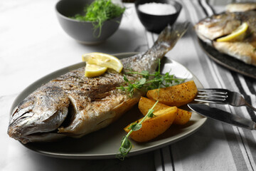 Seafood. Delicious baked fish served with lemon, potato and microgreens on light table, closeup