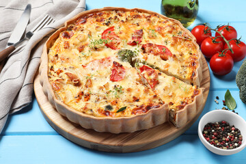 Tasty quiche with tomatoes, microgreens and cheese served on light blue wooden table, closeup