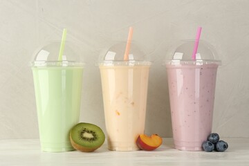 Plastic cups of different tasty smoothie and fresh fruits on white wooden table